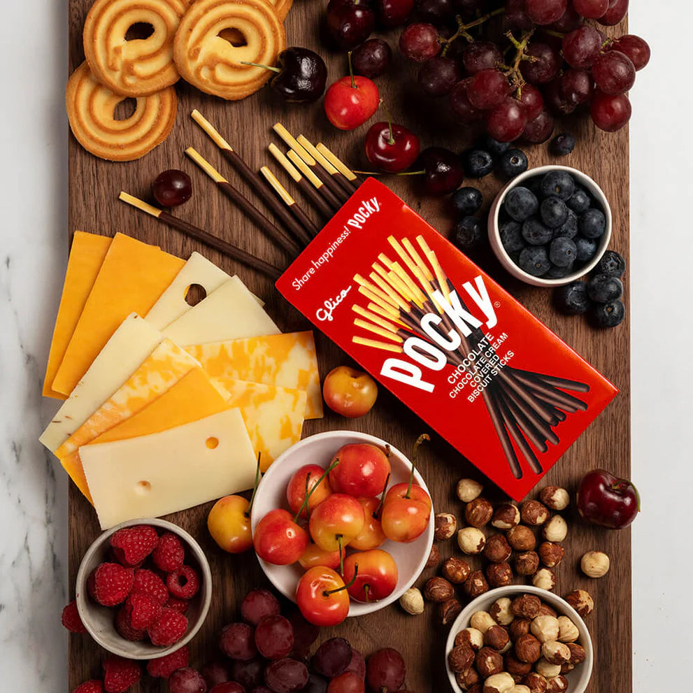 Wooden board with assorted cheeses, fruits, and nuts, featuring a box of Rocky Road chocolate bars.