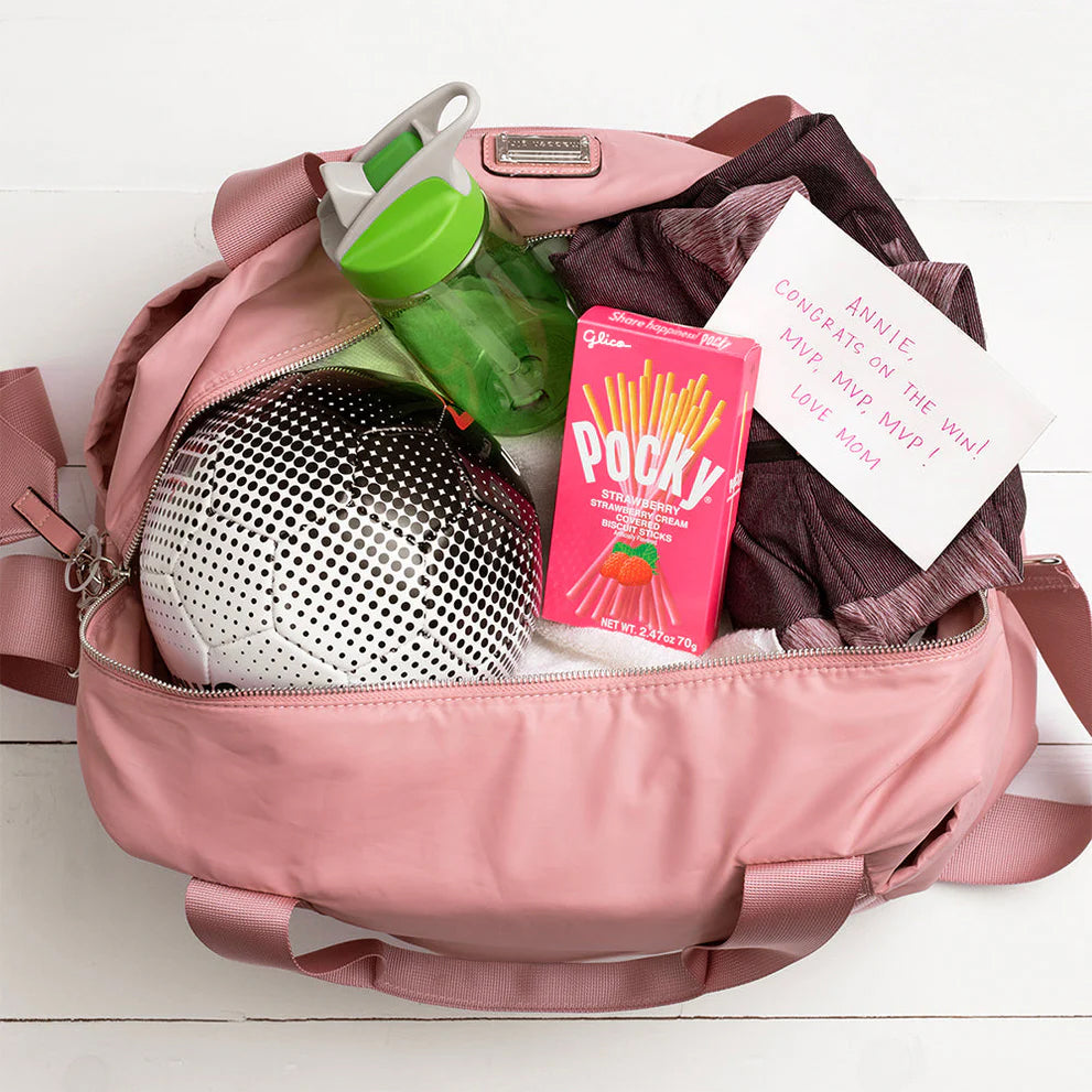 Pink backpack with various items including a disco ball, Pocky, and a card on a white background