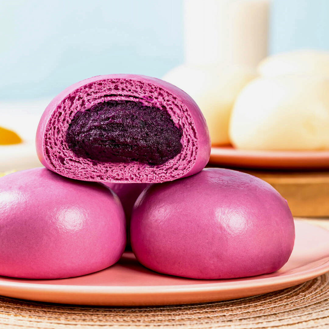 Ube Purple yam bread rolls with one sliced open on a pink plate