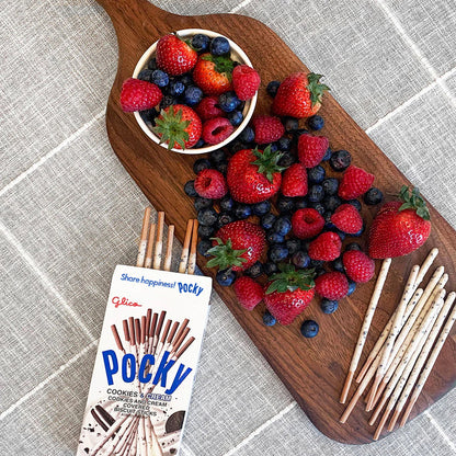 Wooden board with berries, a bowl of berries, and a box of Pocky on a textured surface.