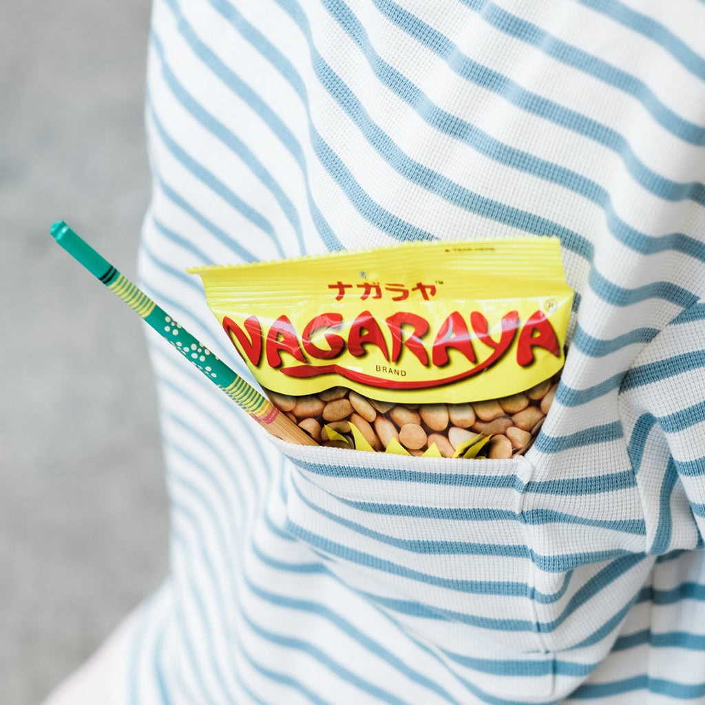 Person wearing a striped shirt with a yellow package of Nagaraya Original Cracker Nuts 160g in the pocket.